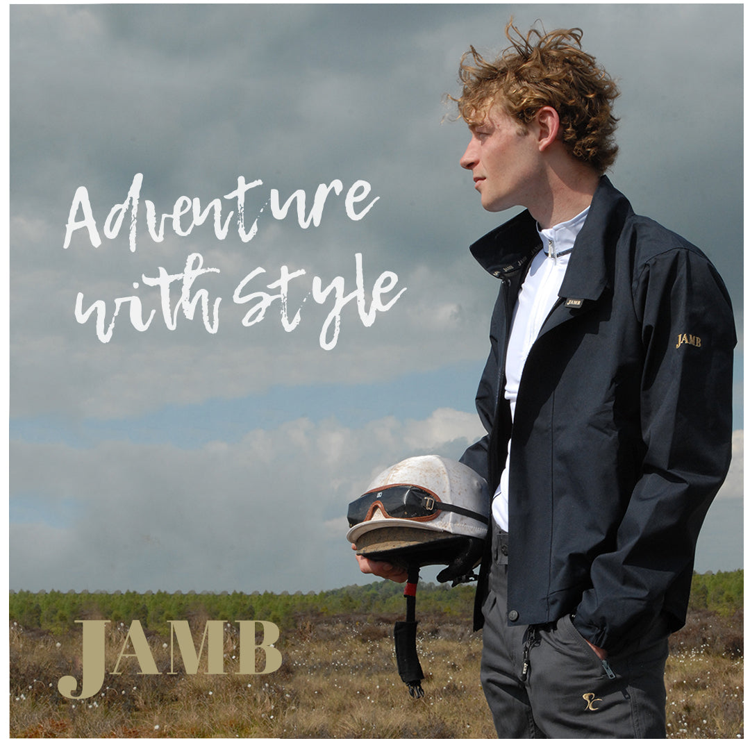 Model wearing a navy JAMB jacket outdoors and holding a riding helmet