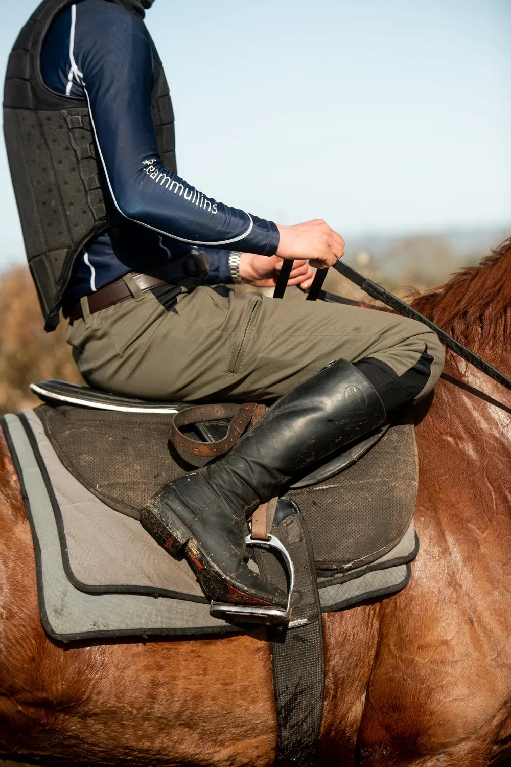 Rider wearing olive breeches and black riding boots on a chestnut horse
